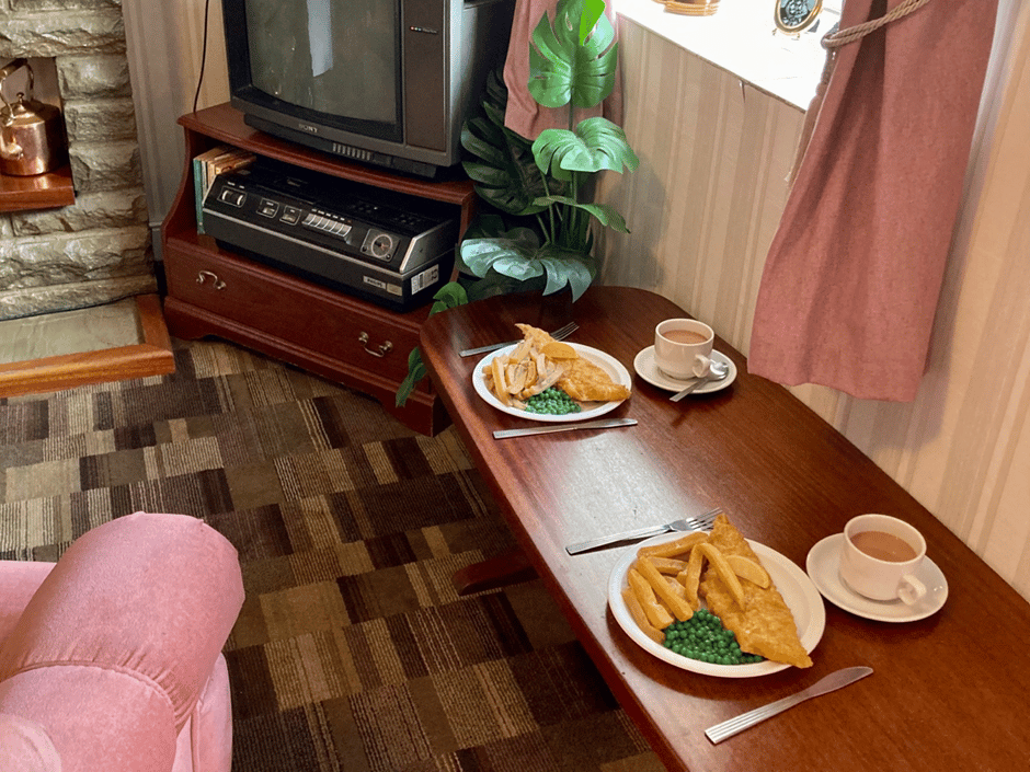 Plate of fish and chips and cups of tea on a table in a living room. This scene is recreated at St Fagans National Museum of History, Cardiff.
